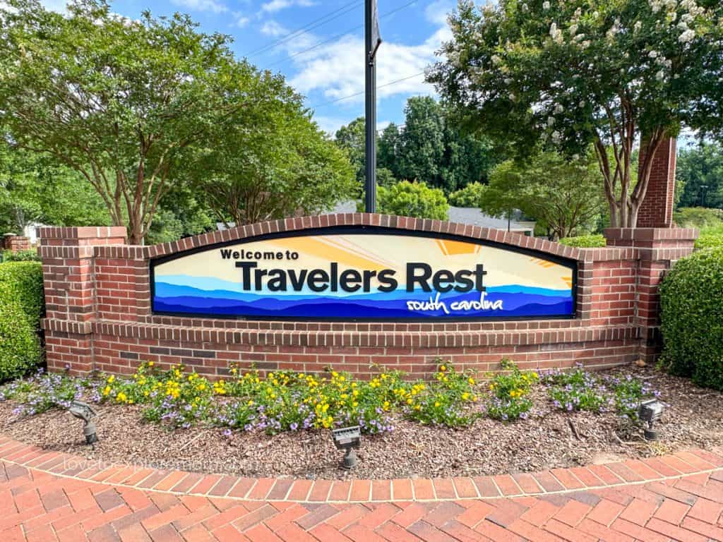 Colorful welcome sign at the entrance of Travelers Rest, South Carolina, adorned with flowers and set against a backdrop of trees.
