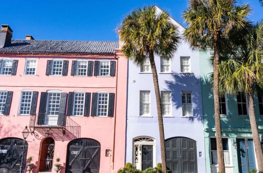 Rainbow Row with a pink, lavender, and green home next to each other with palm trees in the front.