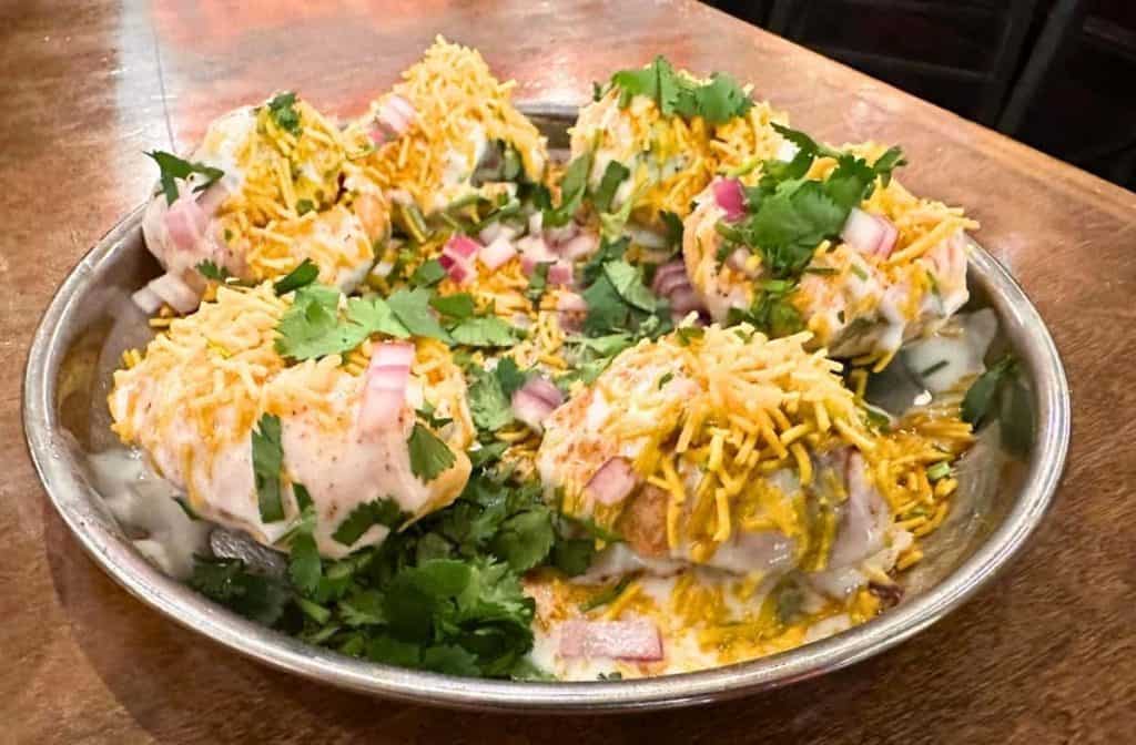 A vibrant plate of Indian street food from Chai Pani in Asheville, NC, garnished with fresh herbs, crispy toppings, and colorful spices.