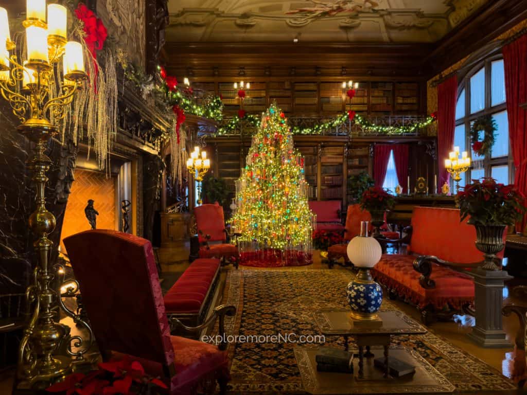 The library at Biltmore Estate adorned with a glowing Christmas tree, garlands, and cozy seating arrangements, highlighting the holiday spirit.