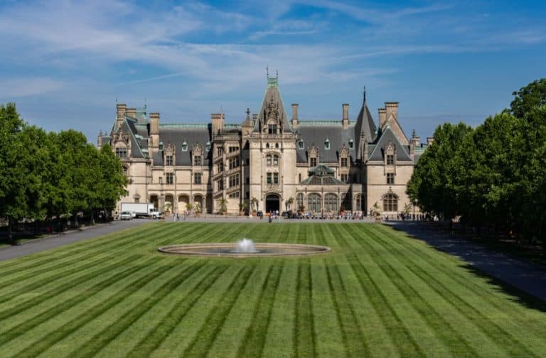 Exterior view of the grand Biltmore Estate in Asheville, NC, surrounded by lush green lawns under a clear blue sky.