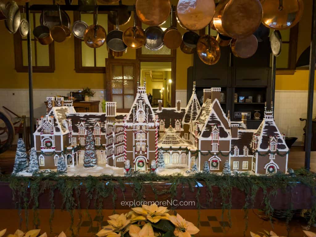 A detailed gingerbread model of the Biltmore House displayed in the estateβs kitchen, surrounded by festive decor and copper cookware.