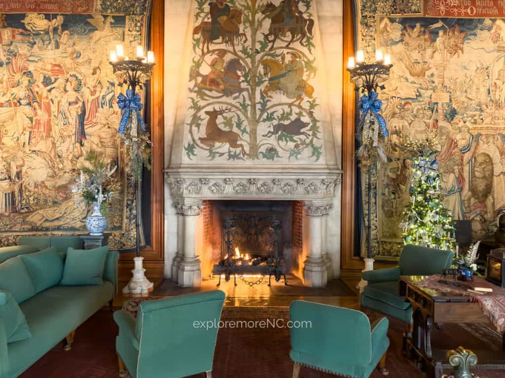 A cozy room at the Biltmore Estate featuring an ornately decorated fireplace, tapestries, holiday garlands, and elegant seating.
