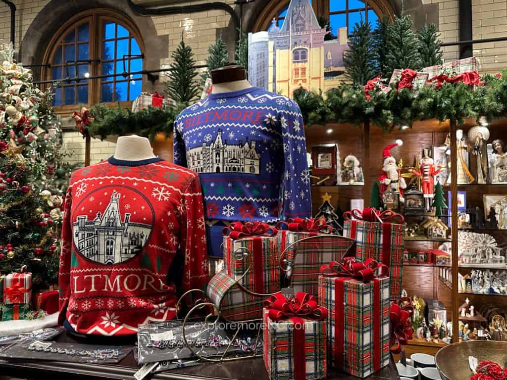 A display of festive Biltmore-themed Christmas sweaters and gift items in a holiday-decorated shop at the estate.