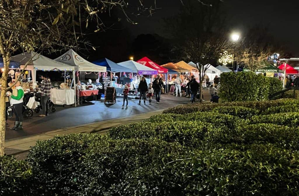 Christmas market booths lit up at night in Huntersville, NC, with families shopping for holiday gifts.