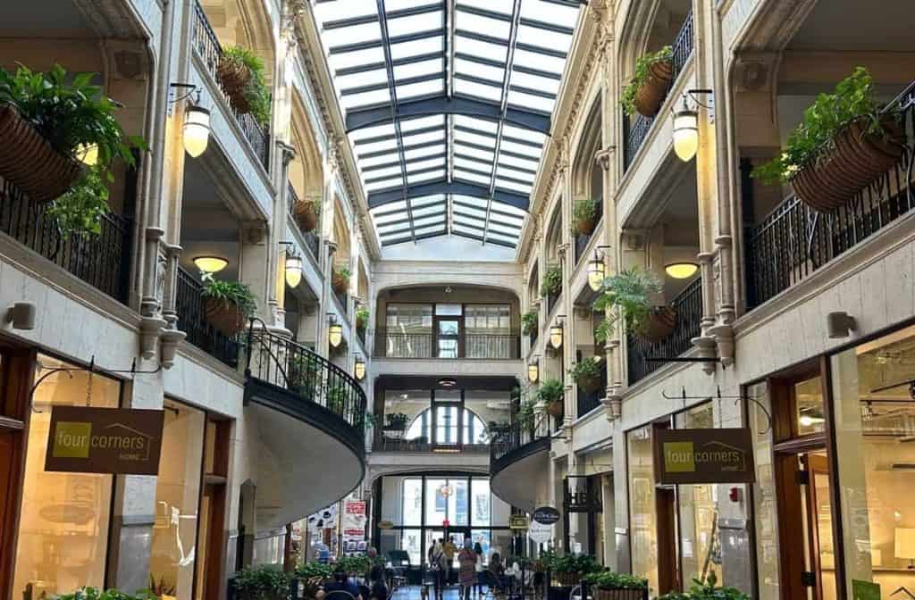A view inside the Grove Arcade in Asheville, NC, featuring its iconic glass ceiling, elegant architectural details, and lush hanging plants.